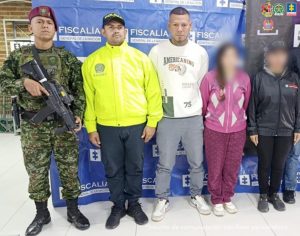  en la imagen se ven dos personas detenidas bajo custodia de un investigador del CTI, un uniformado de la Policía Nacional y otro del Ejército. Detrás suyo un backing institucional.