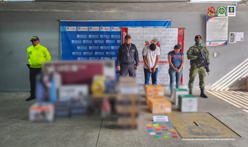 en la imagen se ven dos personas detenidas bajo custodia de investigadores del CTI, Ejército y Policía con los elementos incautados como televisores y otros electrodomésticos.