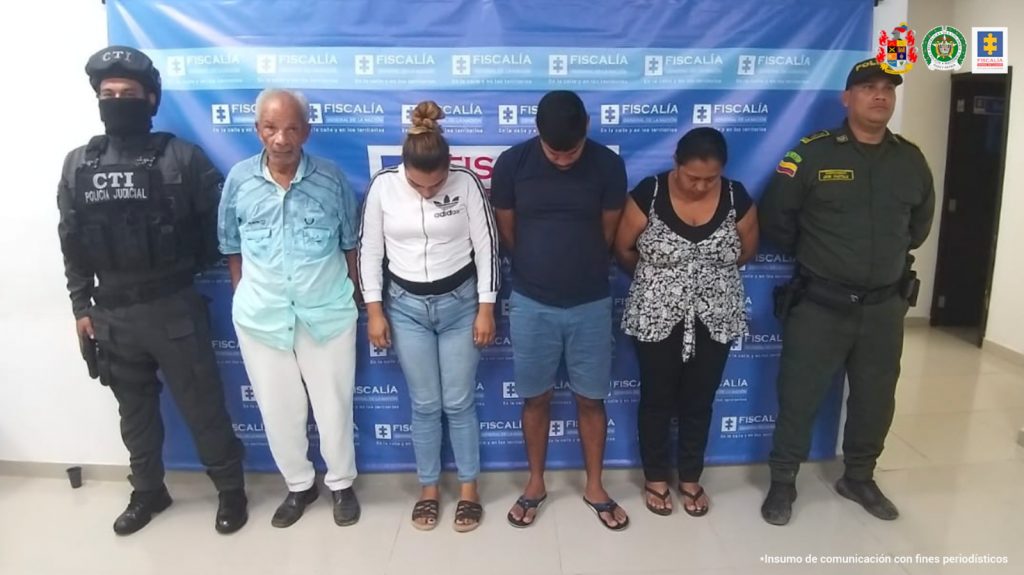 En la imagen se ve un grupo de personas detenidas bajo custodia del CTI y la Policía. Detrás suyo un backing de la Fiscalía.