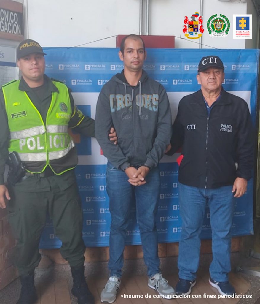 En la imagen se ve un hombre detenido bajo custodia de la Policía y el CTI. Detrás suyo un backing de la Fiscalía.