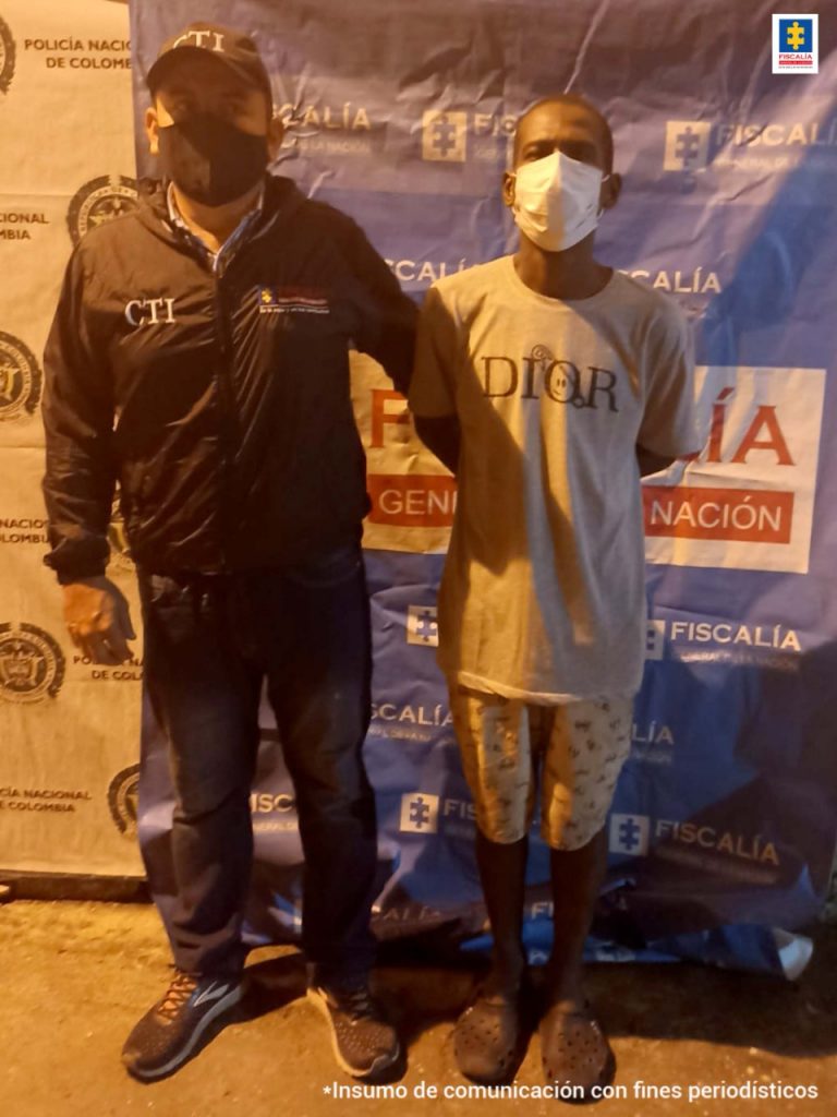 En la imagen se ve un hombre detenido con dos funcionarios de la Policía Nacional. Detrás hay un backing de la misma entidad.