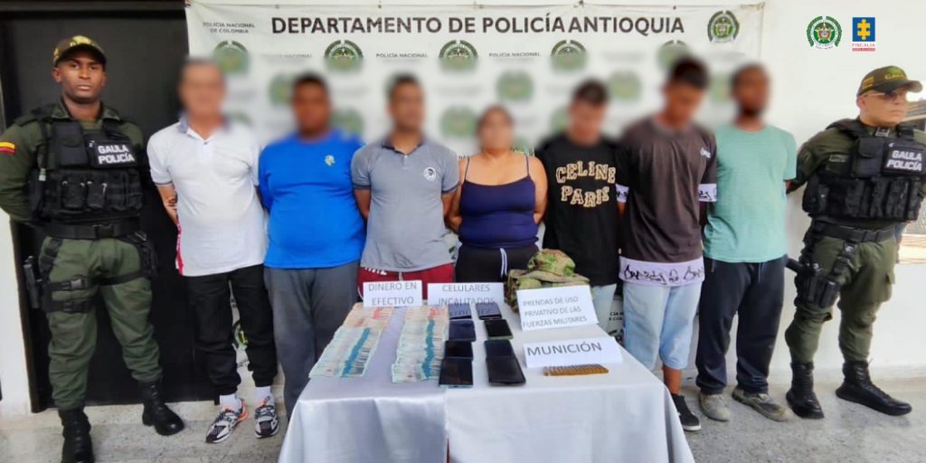 En la imagen están los 7 procesados con dos servidores de la Policía Nacional y una mesa al frente con los celulares, la munición y dinero incautado