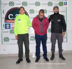 en la imagen se ve una persona detenida bajo custodia de un investigador del CTI y de la Policía Nacional. Detrás suyo un backing de ambas instituciones. 