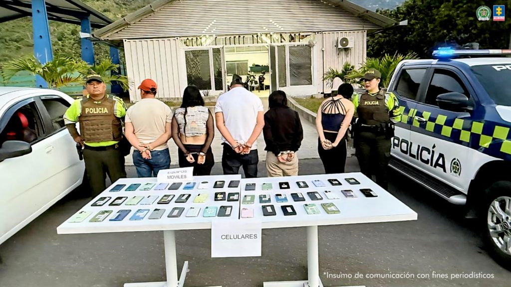 en la imagen se ven varias personas detenidas bajo custodia de la Policía Nacional. Una mesa delante de ellos con elementos incautados.