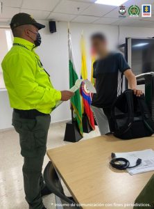 Un agente de la Policía lee sus derechos a un detenido. Al fondo puede verse la bandera de Colombia