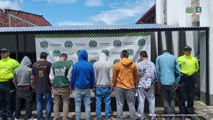 en la imagen se ven dos personas detenidas bajo custodia de dos integrantes de la Policía Nacional.