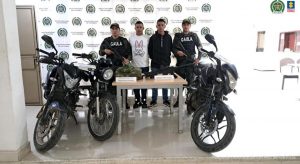 en la imagen se ven dos personas detenidas bajo custodia de integrantes del Gaula de la Policía. Detrás suyo un backing institucional.
