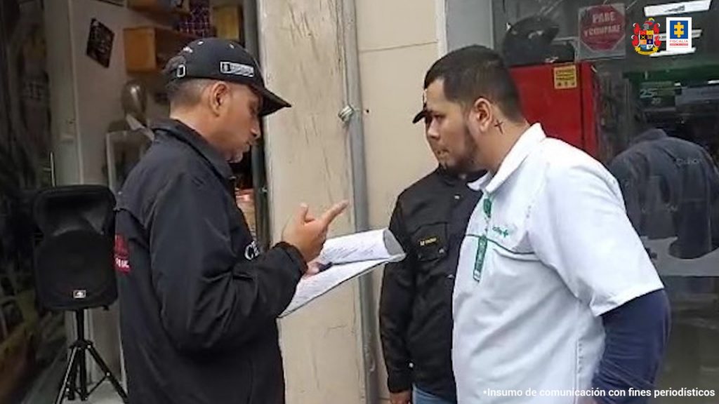 En la imagen se ve una persona a quien le están leyendo los derechos como capturado por parte de un investigador del CTI. Lo acompaña igualmente un servidor del Gaula Militar. Se encuentran en vía pública.