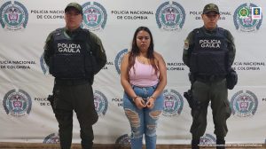 Se observa la capturada de frente y a cada costado un funcionario de Policía Nacional. Atrás un pendón de Policía Nacional