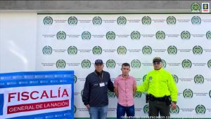 Asegurados dos hombres investigados por homicidio en Caquetá En la imagen se ve una persona detenida bajo custodia de un investigador del CTI y de la Policía. Detrás suyo backings institucionales.