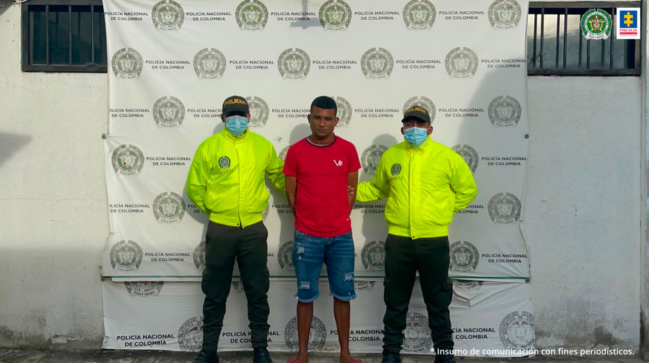 Hombre capturado de camisa roja con las manos atrás y de pie, ubicado en medio de dos uniformados de la Policía Nacional.