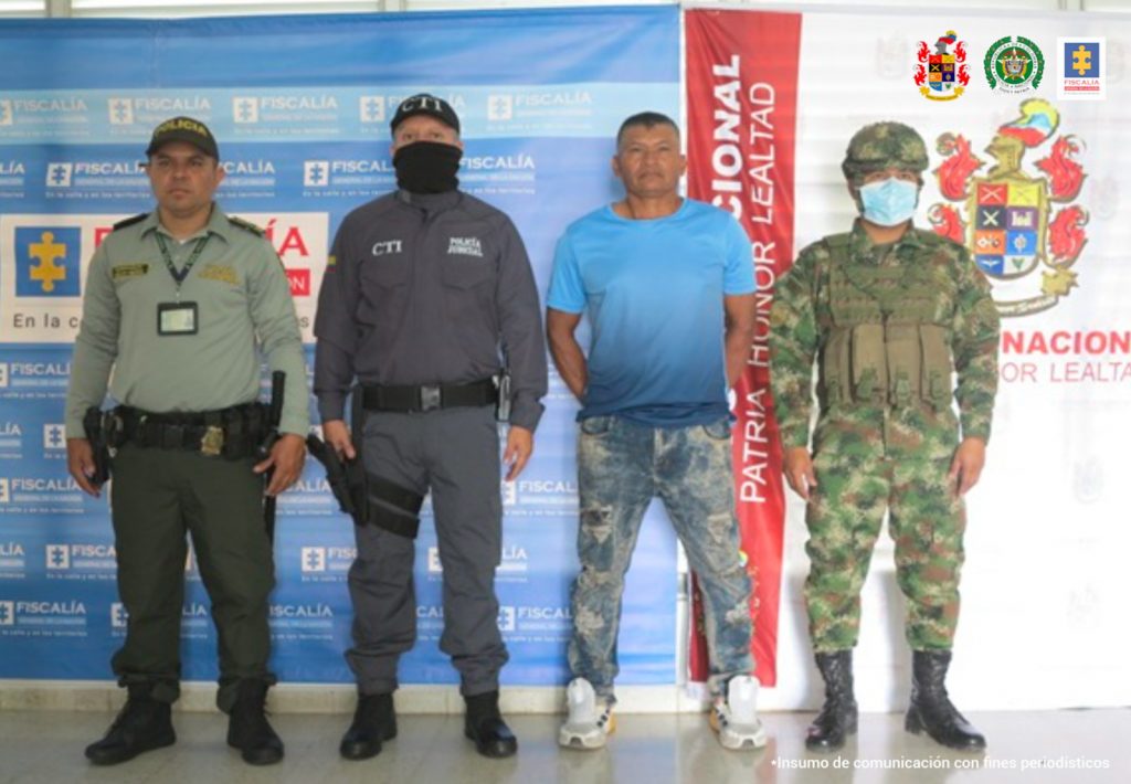 en la imagen se ve una persona detenida bajo custodia de un servidor del CTI, del Ejército y la Policía. Detrás suyo backings institucionales.