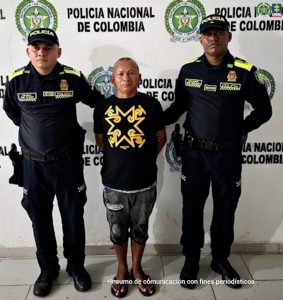 En la imagen aparece una persona de suéter negro, y bermuda de jean, entre dos uniformados de la Policía Nacional.