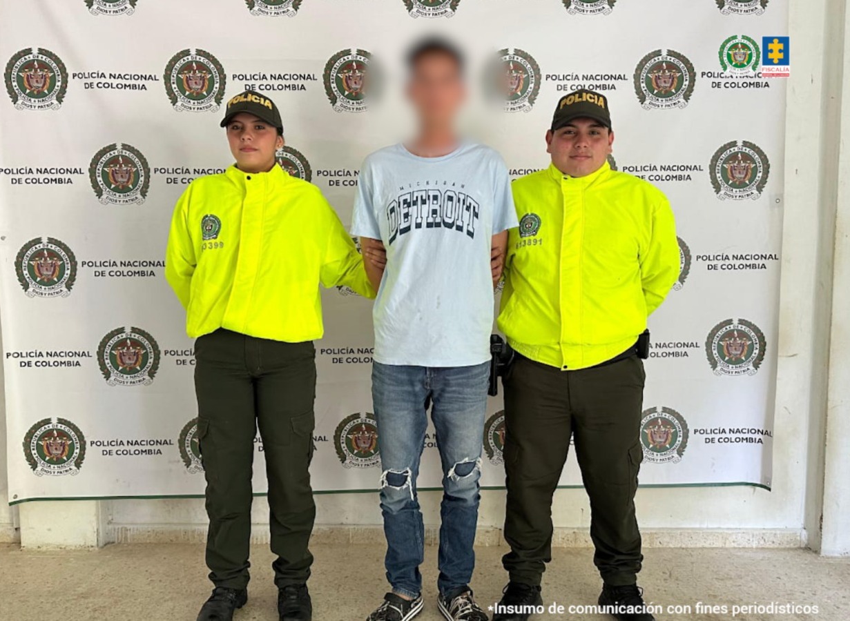 En la imagen se ve un hombre detenido bajo custodia de integrantes de la Policía Nacional.