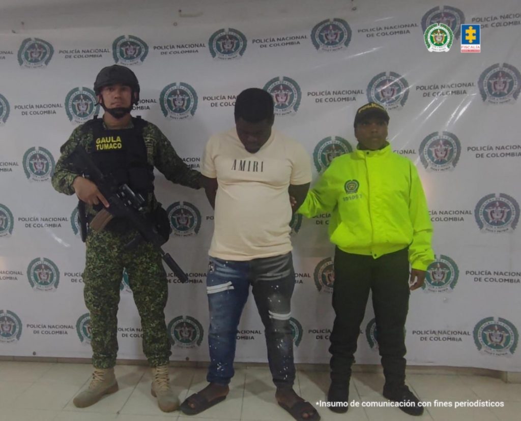 En la fotografía aparece el capturado junto a un funcionario del CTI y  un soldado del Gaula Militar. En la parte superior se observa un banner de la Fiscalía General.