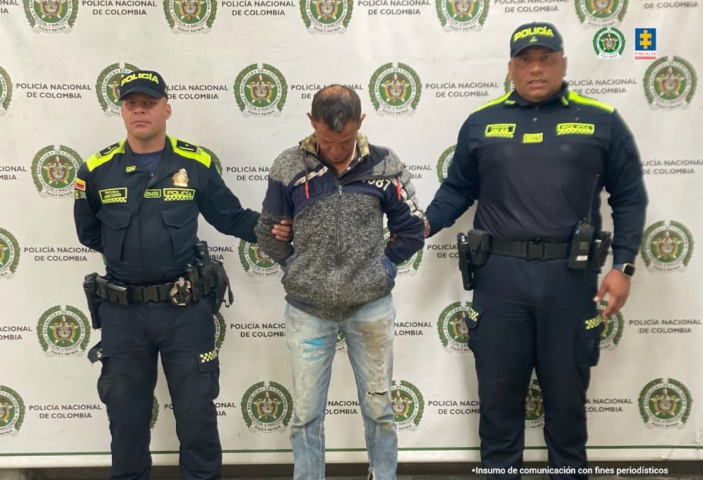 Se visualiza al capturado junto a dos uniformados de la Policía Nacional. Detrás de ellos el banner que identifica a la Policía Nacional.