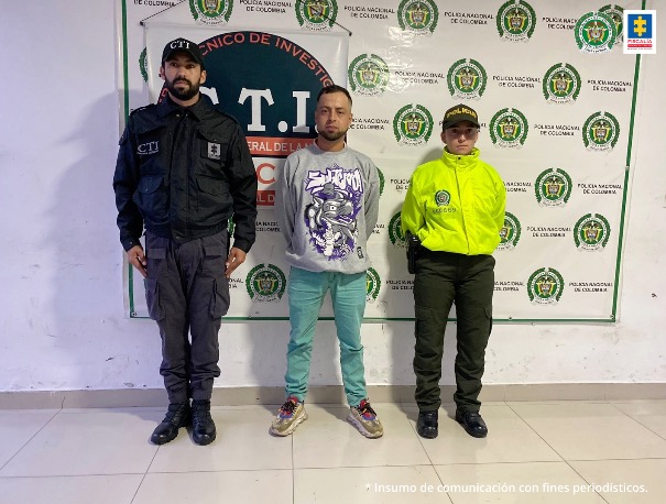 En la imagen se ve una persona detenida custodiada por un uniformado de la Policía Nacional y del CTI. Detrás suyo backings de cada una de las instituciones.