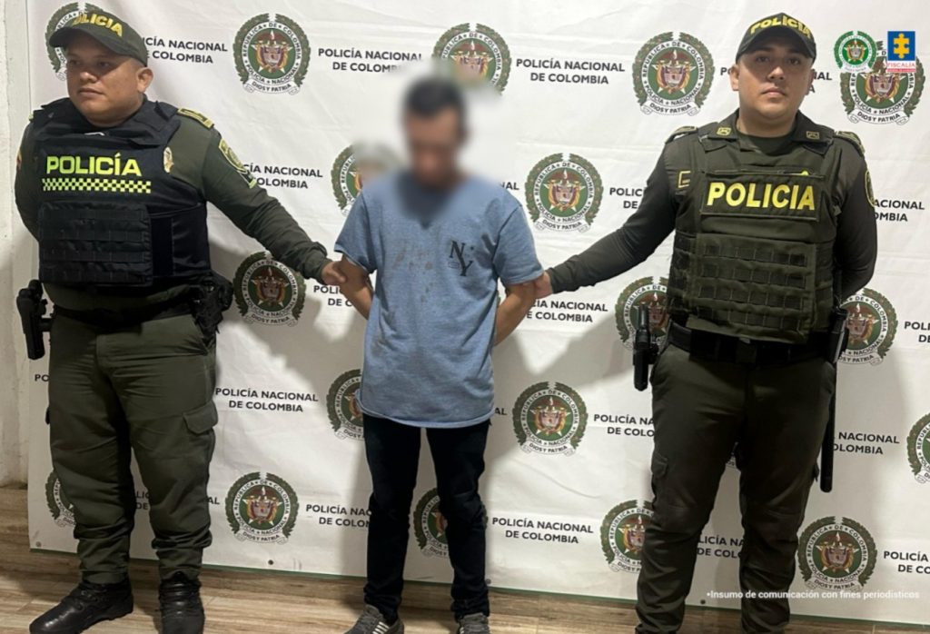 en la imagen se ve una persona detenida bajo custodia de dos integrantes de la Policía Nacional.