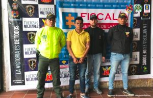 en la imagen se ve una persona detenida bajo custodia de servidores del CTI, Ejército y Policía Nacional. Detrás suyo backings institucionales.  