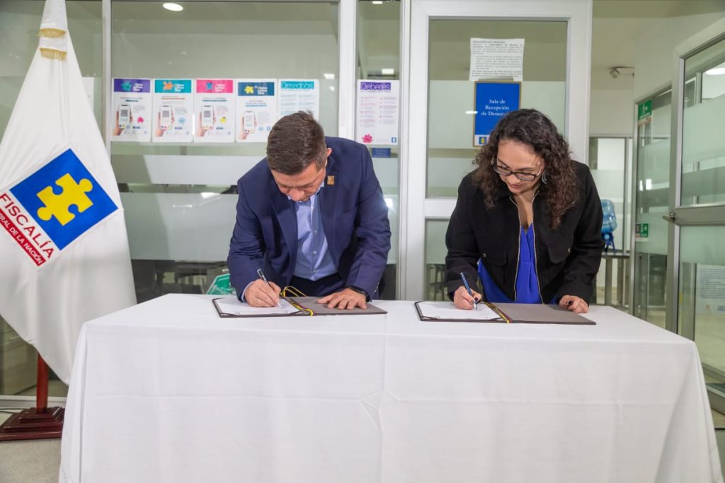 En la imagen se ve al director ejecutivo de la Fiscalía General de la Nación, Alejandro Giraldo López; y la subsecretaria técnica de la Secretaría de Integración Social de Bogotá, Beatriz Juliana Sánchez Calderón, en un acto realizado en el Centro de Atención de Fiscalía (CAF) en el sector de Paloquemao, en Bogotá, firmando un acuerdo sin precedentes que permitirá articular capacidades para identificar casos en los que las mujeres víctimas de violencia de género podrían estar en riesgo de feminicidio.