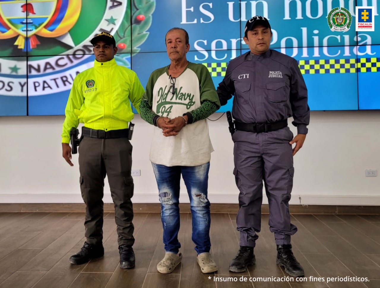 En la fotografía aparece un capturado, junto a personal de Policía Nacional y  Fiscalía General de la Nación. En la parte posterior de la imagen se ven banners de Policía Nacional y la Fiscalía General de la Nación.    