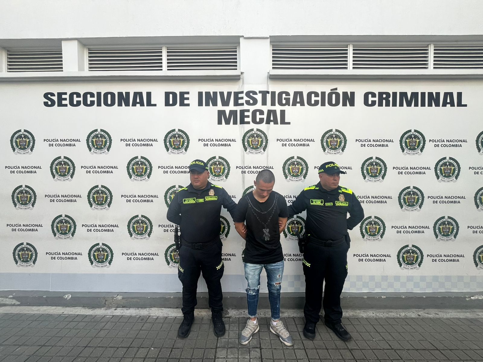 En la fotografía aparece de pie, con los brazos atrás y la cabeza inclinada hacia abajo Cristian Felipe Peña Castillo. Viste con camiseta de mangas cortas, de color negro; jean azul desgastado y zapatillas azul claro con blanco. A sus extremos hay uniformados de la Policía Nacional. Detrás de ellos hay un pendón institucional de la Policía.