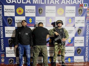 capturado de espaldas custodiado por investigador del CTI de la Fiscalía y militar. Detrás banner de grupo Gaula Militar y Fiscalía.