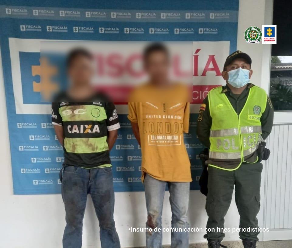 En la fotografía aparecen dos hombres capturados, junto a personal de la Policía Nacional. En la parte posterior de la imagen se ve un banner de la Fiscalía con texto alternativo.