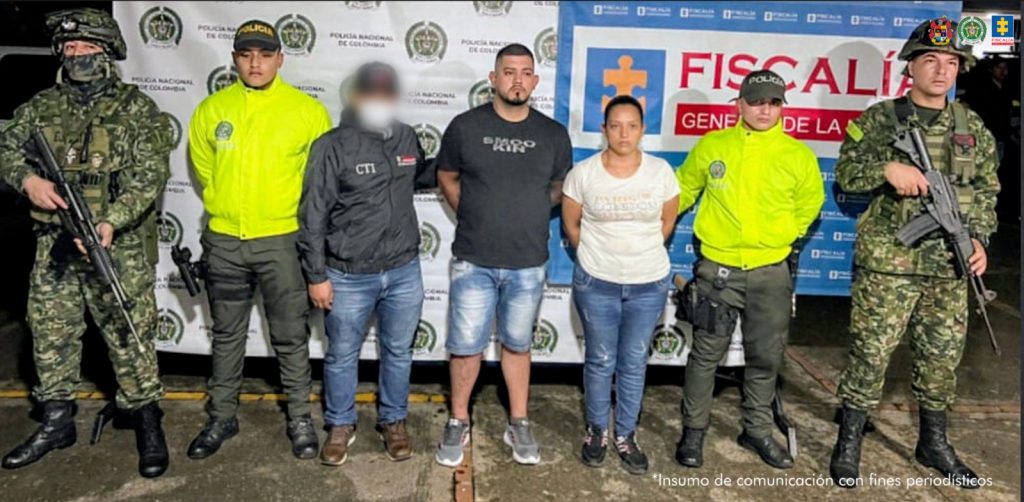 En la fotografía aparecen los dos capturados junto a un servidor del CTI, dos uniformados de la Policía y dos soldados del Ejército. En la parte superior está un banner de la Fiscalía General y otro banner de la Policía Nacional.