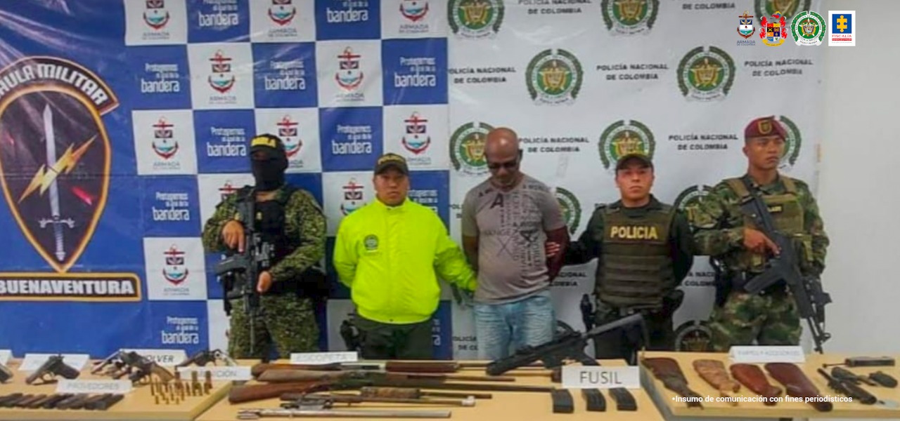 En la fotografía se observa al capturado junto a una unidad del Gaula Militar, dos agentes de la Policía Nacional y un soldado de las Fuerzas Especiales del Ejército. En la parte posterior se observa una mesa con pistolas, revólveres, escopetas, culatas de escopeta y munición. 