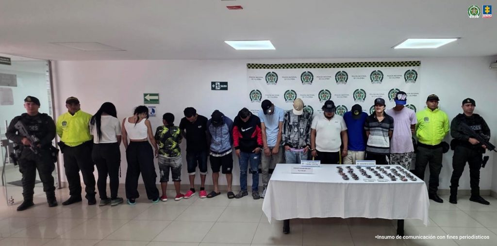 En la fotografía se aprecian en hilera y esposados entre sí los presuntos integrantes del grupo delincuencial La Vieja. Tres de ellos, ubicados en el extremo izquierdo de la fotografía, dan la espalda a la cámara. El resto tiene inclinada la cabeza hacia abajo. En los extremos hay uniformados de la Policía Nacional. Delante de ellos hay una mesa, con mantel blanco y sobre ella hay varias bolsas plásticas transparentes con contenido oscuro. Detrás de ellos hay un pendón institucional de la Policía.