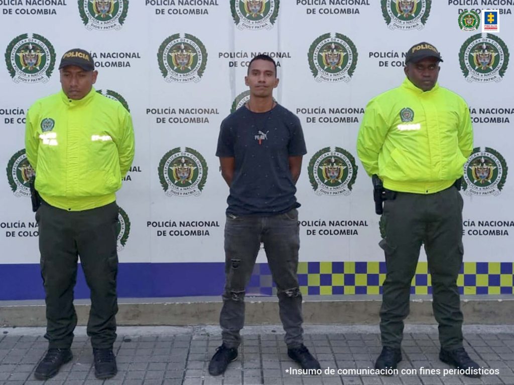 En la fotografía se aprecia a Diego Armando Hurtado Ortiz, de pie y con los brazos atrás. Viste camiseta negra de manga corta con estampado en el pecho de un puma y la palabra ‘Puma’ en blanco; asimismo, pantalón y zapatos negros. A lado y lado de él hay uniformados de la Policía Nacional. Detrás de ellos hay un pendón institucional de la Policía.