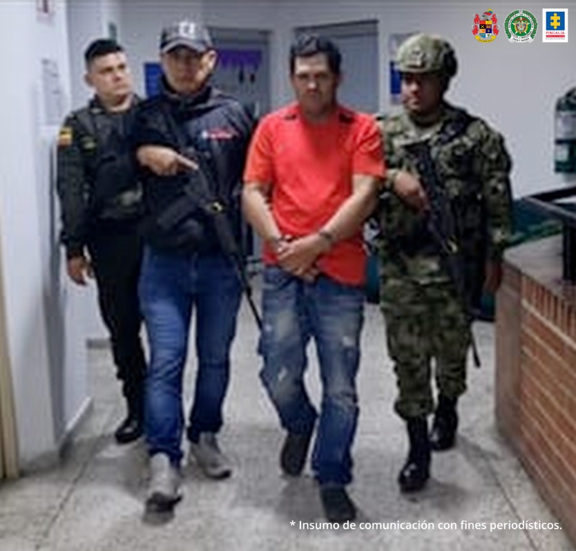 En la fotografía se aprecia a Héctor Fabio Agudelo Franco, en acción de caminata por un pasillo y con los brazos adelante esposados. Viste camiseta roja de manga corta con franjas negras a la altura del cuello; jean azul desgastado y zapatos negros. Al lado derecho de él hay un servidor del CTI de la Fiscalía y un uniformado de la Policía Nacional. A su izquierda hay un uniformado del Ejército.