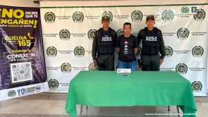 El capturado se encuentra en custodia por dos uniformados del Gaula de la Policía Nacional. En la foto se observa una mesa blanca y un celular incautado.