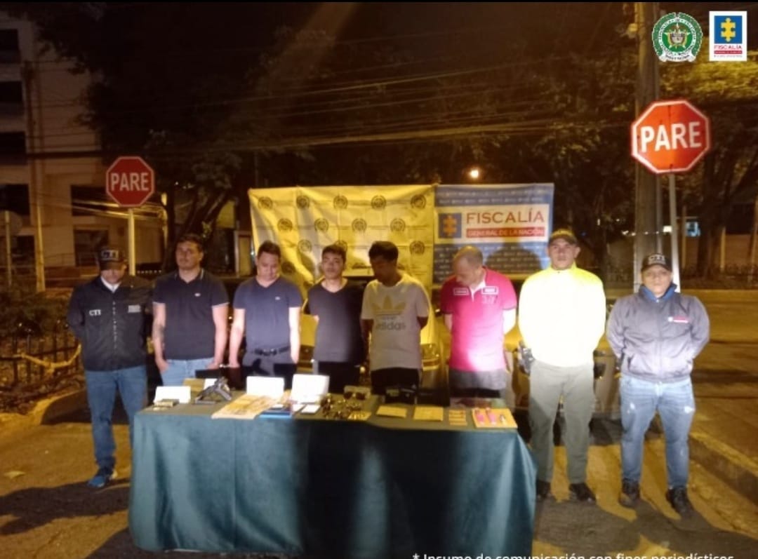 En la fotografía se observan los 5 capturados junto a dos agentes de la Sijin de la policía metropolitana. En la parte posterior se observa una mesa con relojes, joyas de oro, dinero, armas de fuego, billeteras.