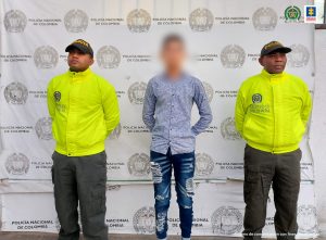 En la imagen está el procesado entre dos uniformados de la Policía Nacional. Tiene las manos hacia atrás esposadas. De fondo está el backing de la Policía.