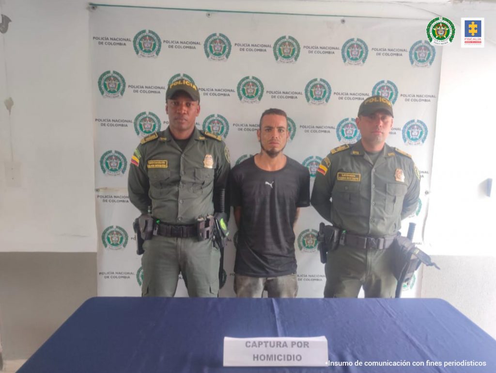 e observa el capturado en el centro y a cada costado un funcionario de Policía Nacional. Al fondo un pendón de Policía Nacional