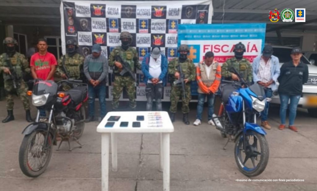 En la fotografía aparecen cinco hombres capturados, acompañado de dos uniformados del Gaula Militar. En la parte posterior dos banners con logos de la Fiscalía y el Ejército Nacional. 