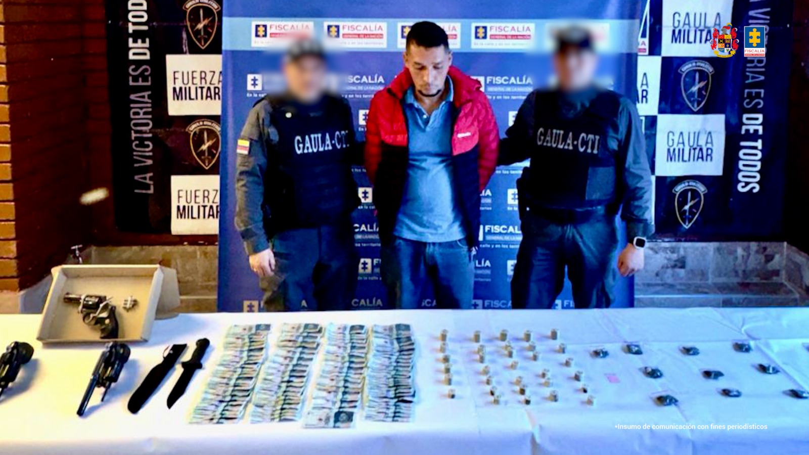 El capturado aparece en el centro de la imagen, con un banner de la Fiscalía de fondo y dos personas del CTI a cada lado. 