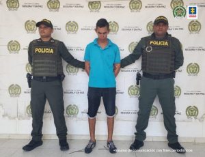 En la fotografía aparece un hombre capturado, acompañado de dos uniformados de la Policía. En la parte posterior un banner con logos de la entidad.