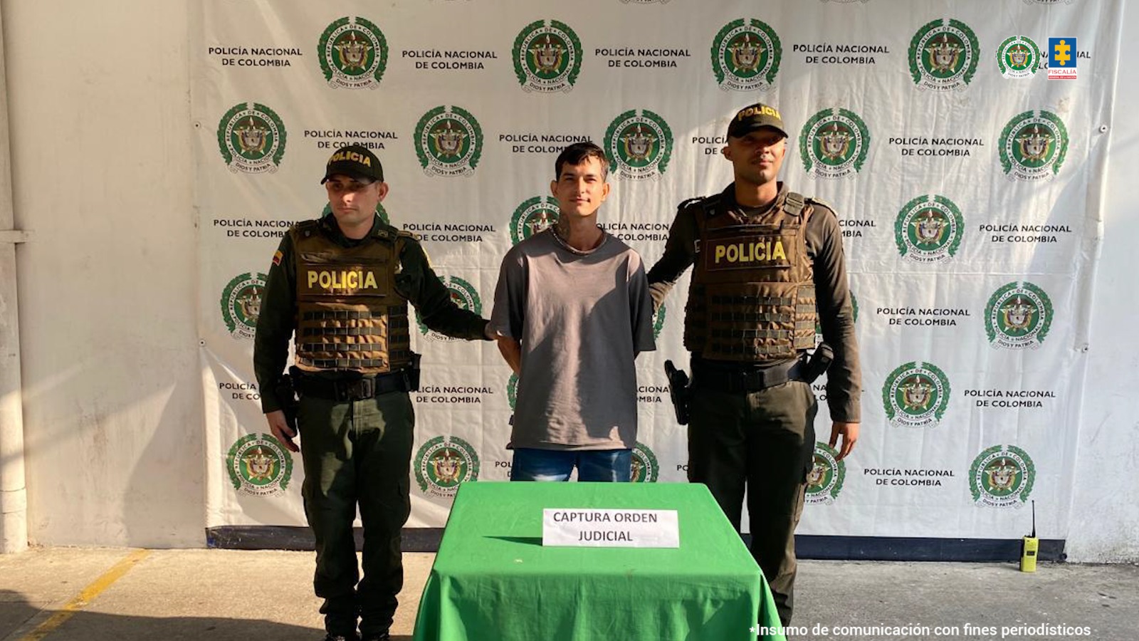 El hombre capturado aparece en el centro de la imagen, rodeado de dos miembros de la Policía. Al fondo puede verse un backing con logos de la Policía. 
