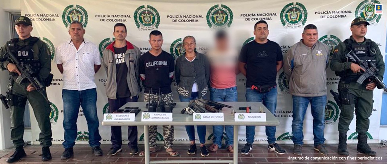 En la fotografía aparecen los 6 capturados junto a dos unidades del Gaula de la Policía. En la parte posterior se observa una mesa con armas de fuego, munición, teléfonos celulares y radios de comunicaciones