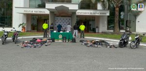 Se observan 4 capturados en fila y a cada costado un funcionario de Policía Nacional.  Al frente una mesa con material incautado al igual que objetos incautados ubicados en el piso a los lados de la mesa.  Igualmente, se observan cuatro motocicletas.