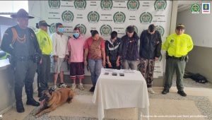 Se observan seis personas capturadas en fila y a un costado dos uniformados de Policía Nacional y un canino de Policía Nacional y al otro costado un funcionario. Al fondo pendón de Policía Nacional