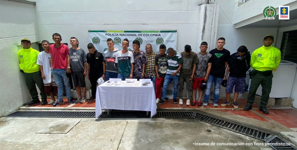 Se observan 14 personas capturadas en fila y a cada extremo un uniformado de Policía Nacional. Adelante una mensa con material incautado y atrás un pendón de Policía Nacional