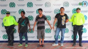 Se observan tres personas capturadas en fila y a cada costado un uniformado de Policía Nacional. Al fondo pendón de Policía Nacional
