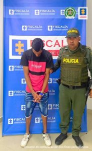 Se observa al procesado junto a uniformado de la Policía Nacional. Detrás se ubicó el banner que identifica a la Fiscalía General de la Nación.