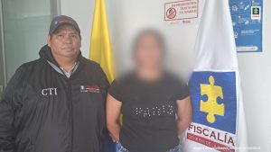 mujer capturada, junto a investigador del CTi Cundinamarca, a su lado izquierdo, esta la bandera de la Fiscalía General de la Nación 