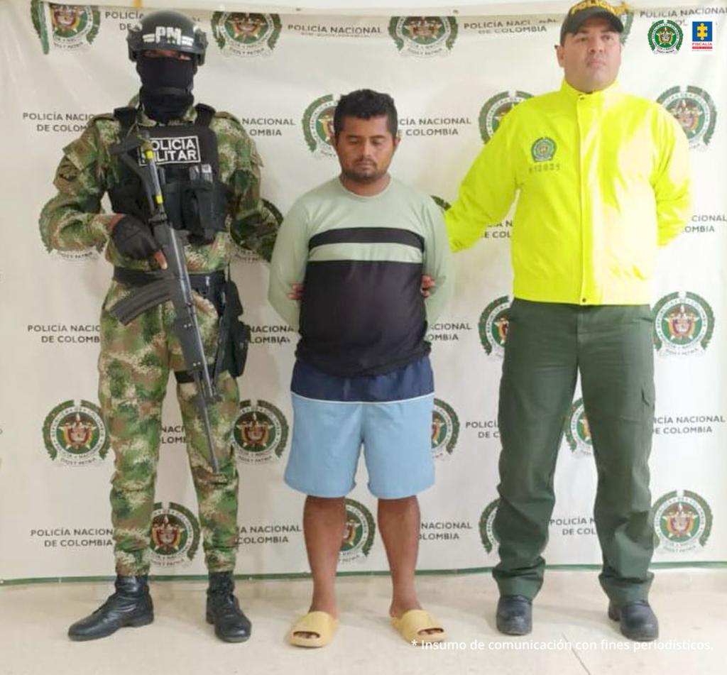 En la fotografía se observan tres personas una de ellas el capturado, y dos integrantes de la policía nacional custodiándolo.