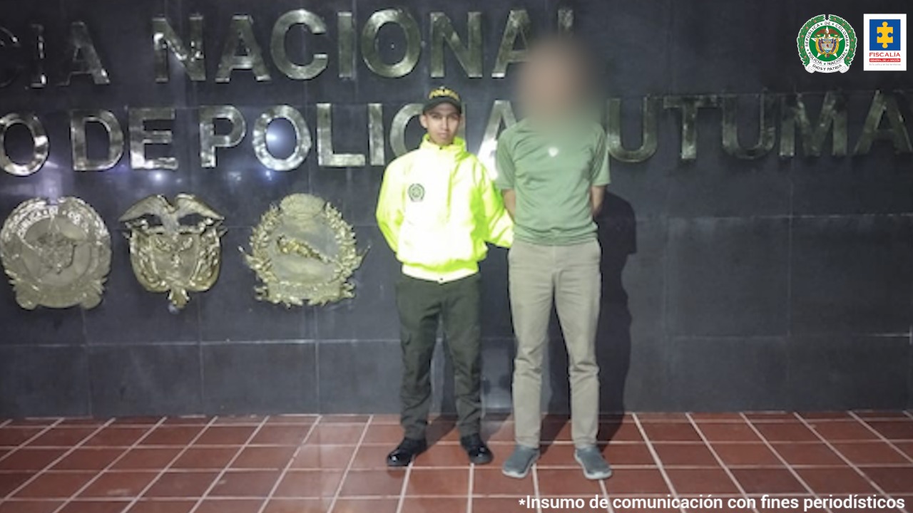 En la fotografía aparece un capturado junto a personal de Policía Nacional. En la parte posterior de la imagen se ven banners de Policía y la Fiscalía General de la Nación.     